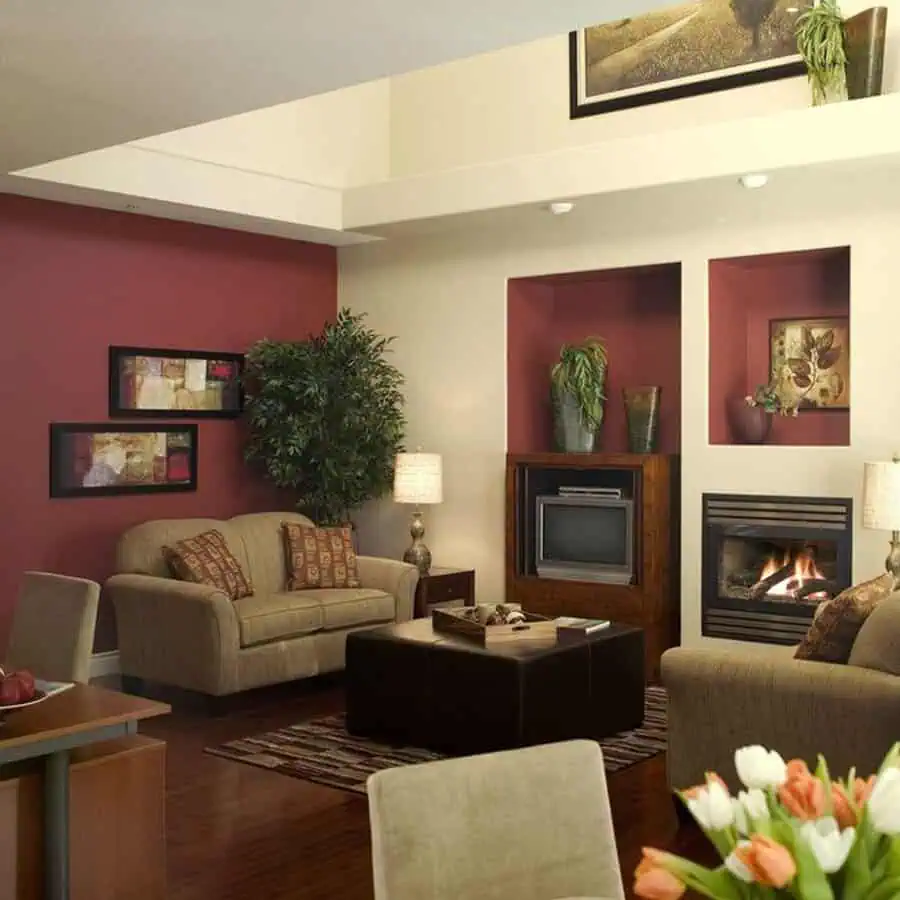 Cozy living room with beige sofas, burgundy accent walls, a fireplace, and warm, ambient lighting.