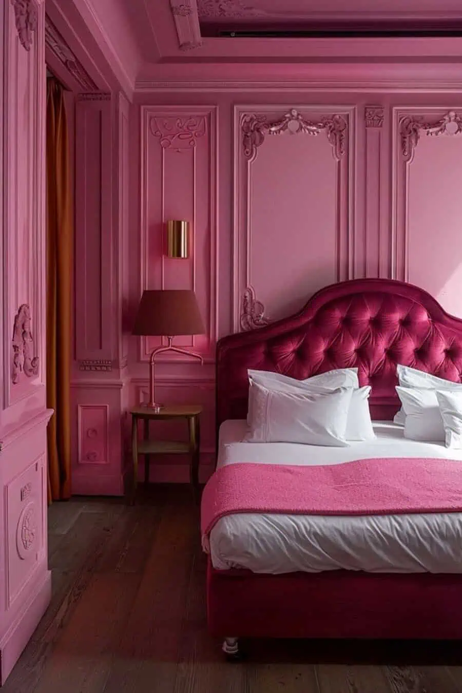 A luxurious bedroom with pink walls, ornate molding, a tufted red headboard, a double bed with white bedding and a pink blanket.