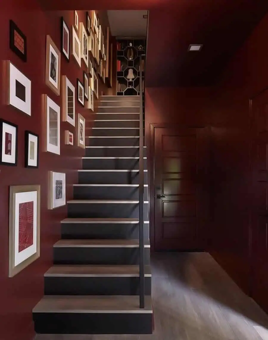 Contemporary staircase with burgundy walls adorned with framed artwork, leading to an upper-level hallway.