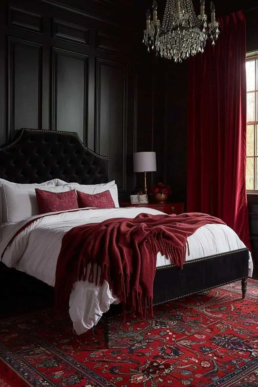 Elegant bedroom with black paneled walls, a tufted headboard, rich red accents, and a crystal chandelier.