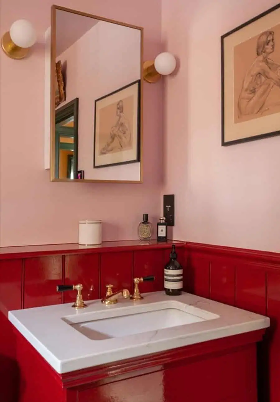 A bathroom with red wainscoting, a white sink with gold faucets, and a rectangular mirror above.