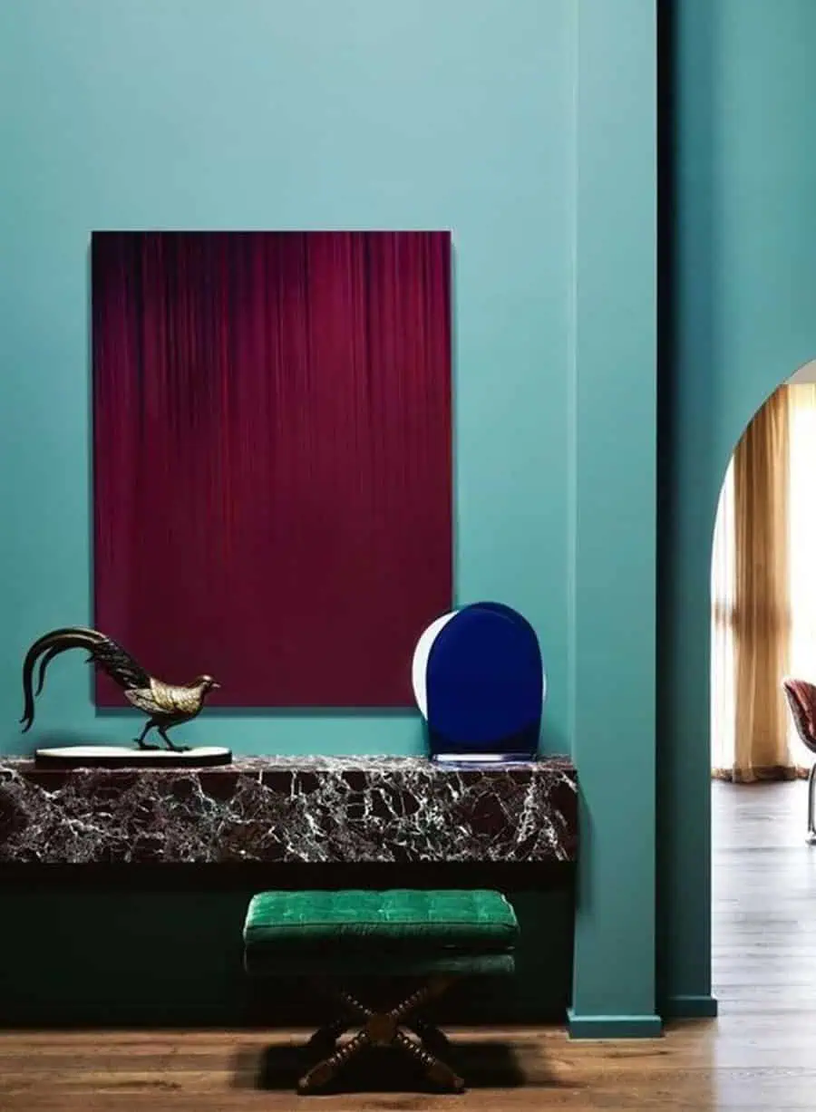 Elegant interior with teal walls, a marble console table, green velvet stool, and a red gradient artwork