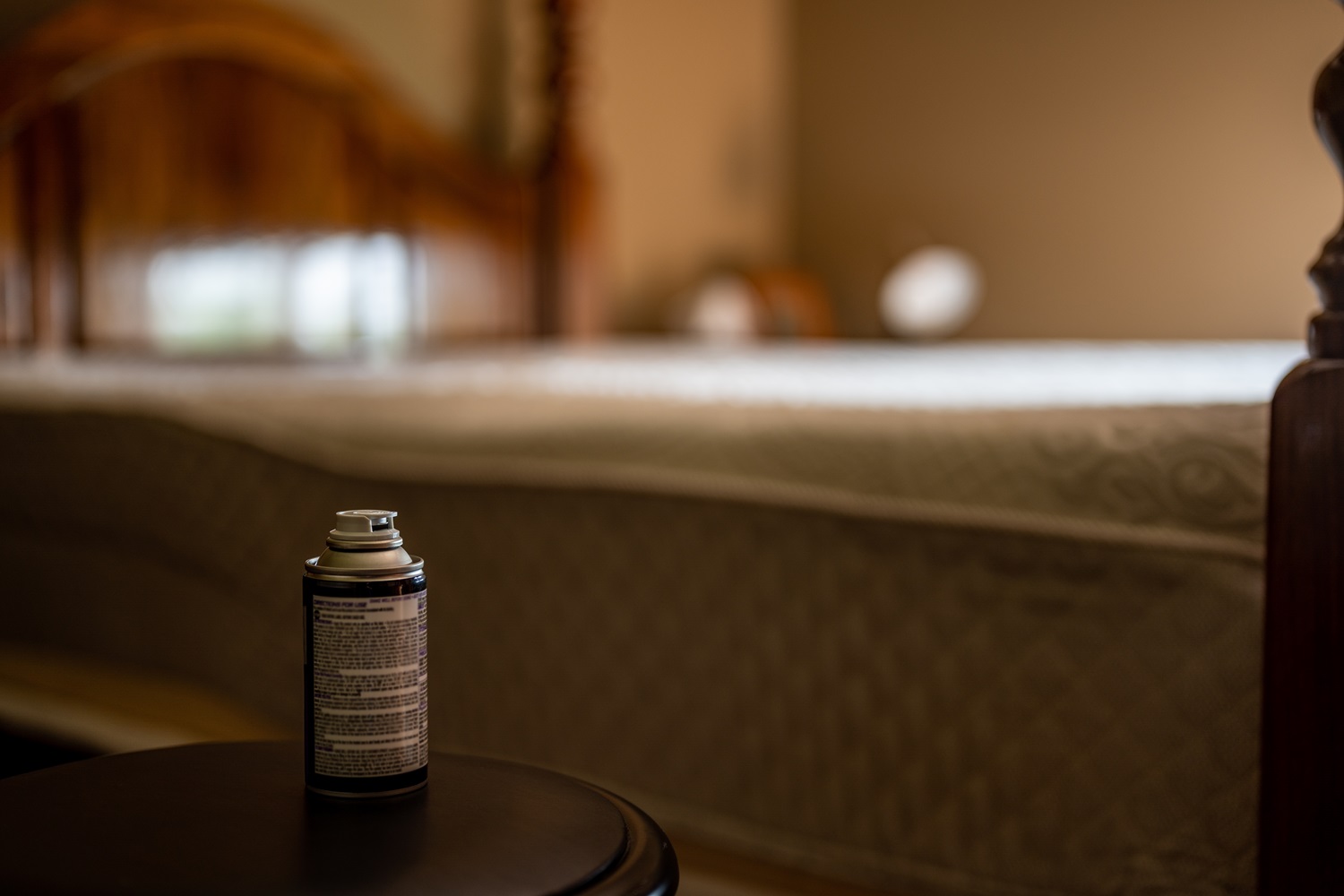  A Commercial Fly Repellent spray can on a small table in a room with a bed in the background