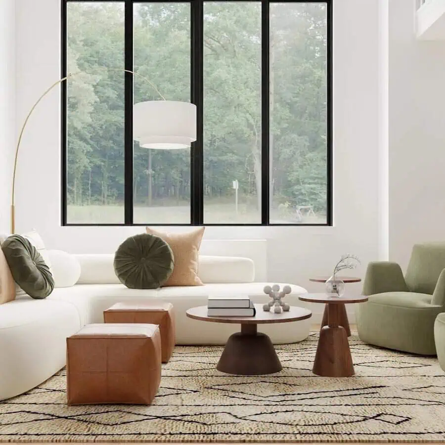 A modern living room with large windows, white sofa, green and brown cushions, and geometric wooden tables on a patterned rug