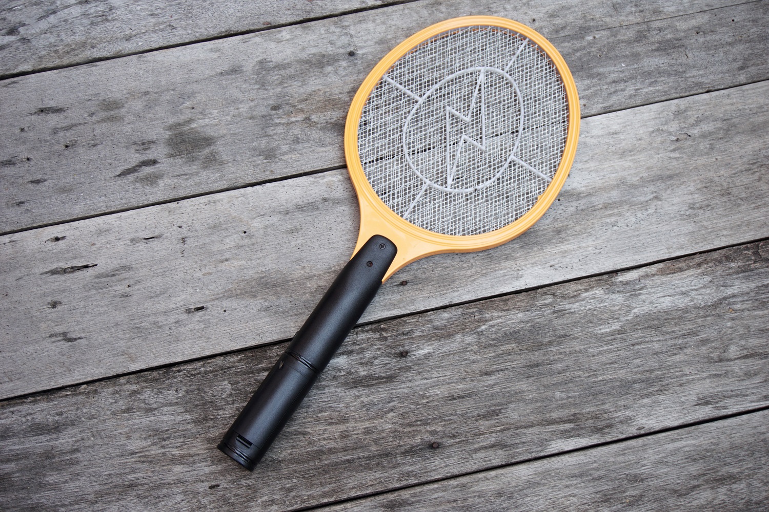 Yellow electric fly swatter lying on a wooden surface