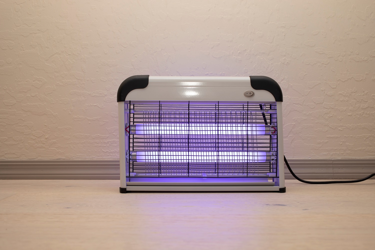 Electric bug zapper with glowing purple light against a beige wall