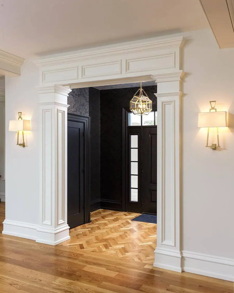 An elegant entryway with white molding, a wooden floor, and a hanging light.