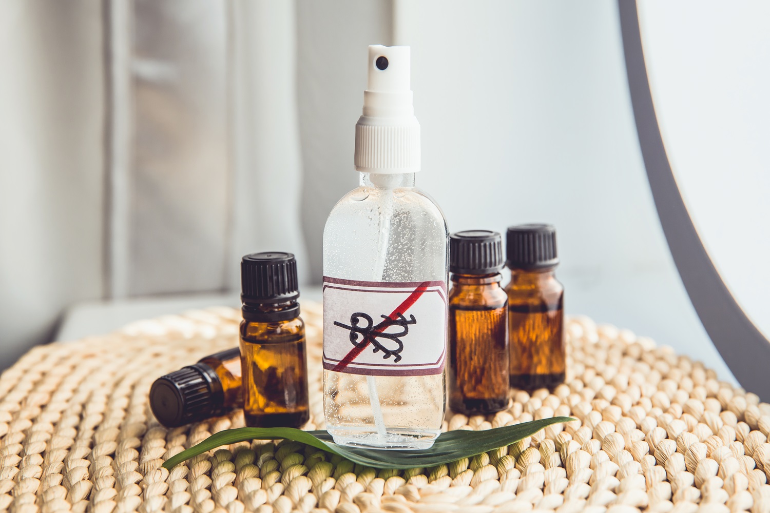 Spray bottle with an anti-bug label surrounded by small amber bottles on a woven mat