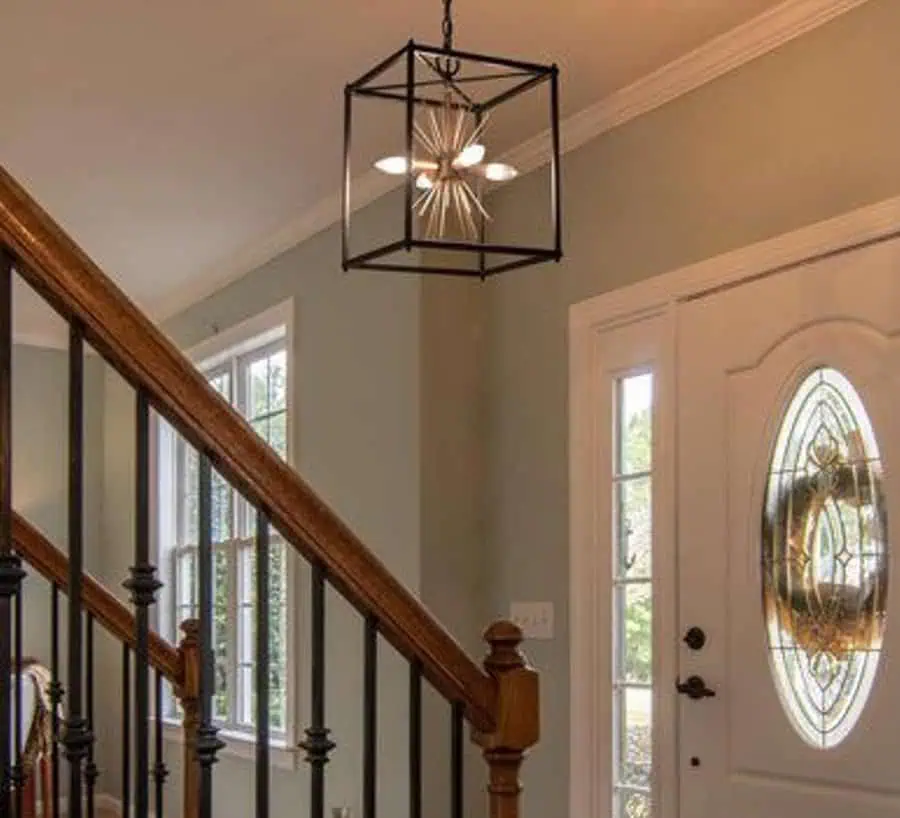 A hallway featuring a staircase with wooden railings and a black chandelier hanging from the ceiling