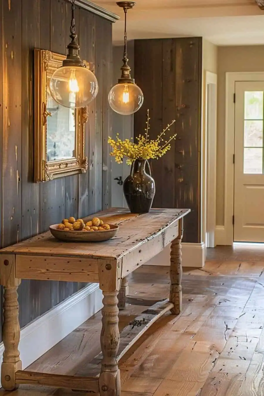 Rustic hallway featuring a wooden table, hanging lights, decorative mirror, vase with flowers, and bowl of potatoes