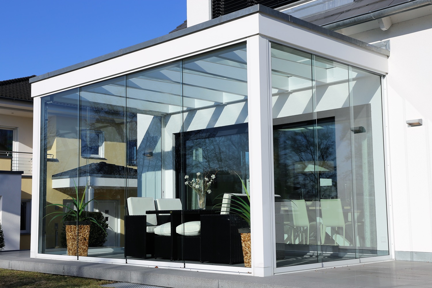 Modern glass-walled sunroom featuring white furniture and potted plants