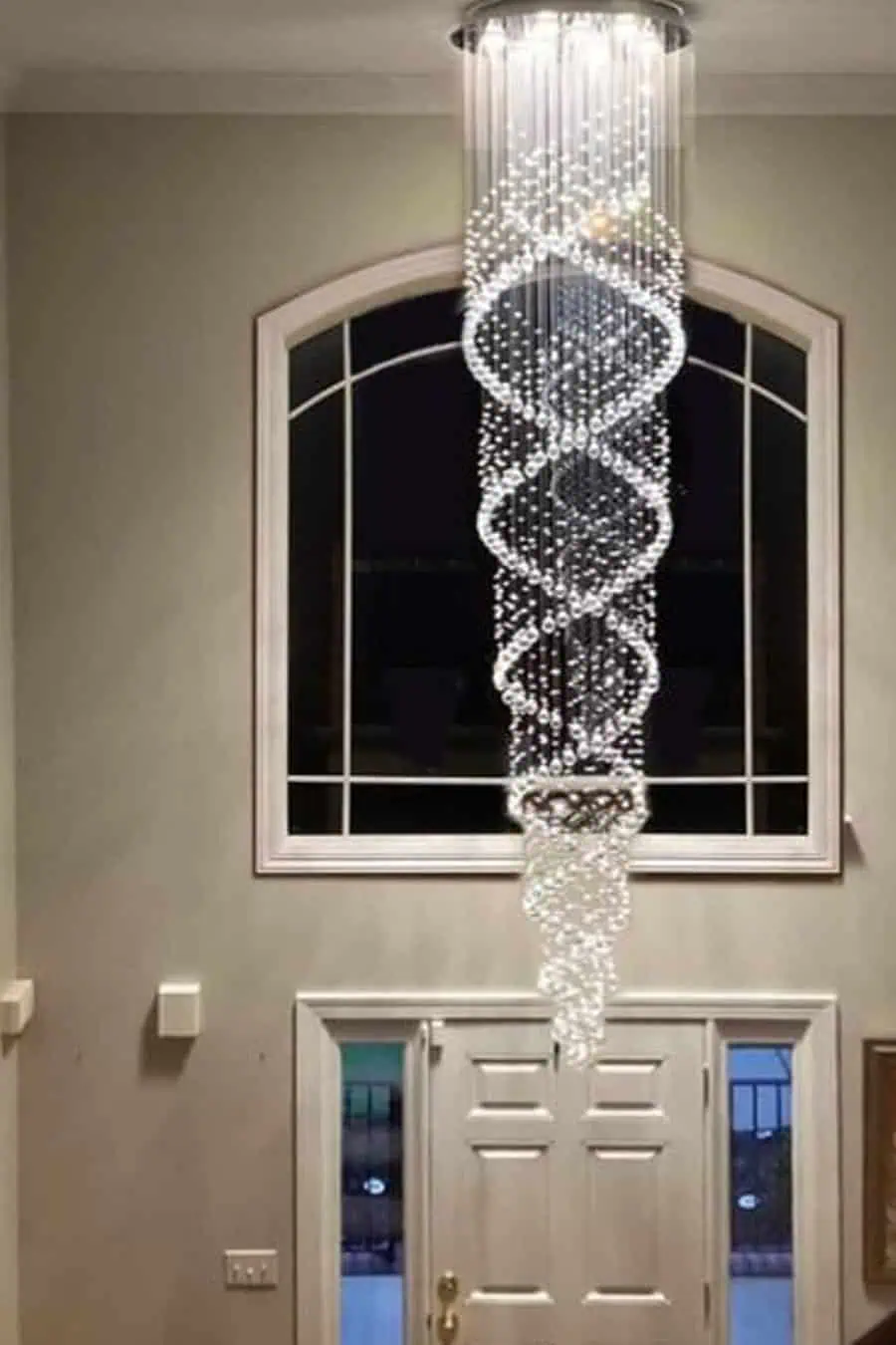 Elegant spiral crystal chandelier hanging in a high-ceilinged entryway with a large arched window above a front door