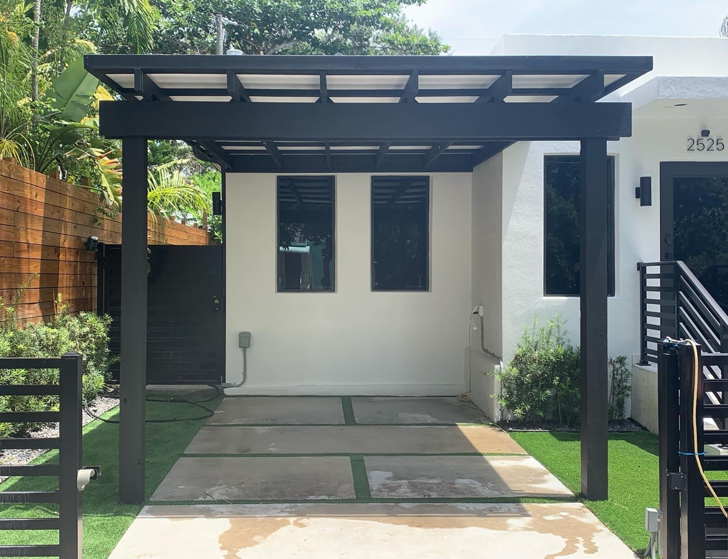 A modern carport with a black pergola structure in front of a white house