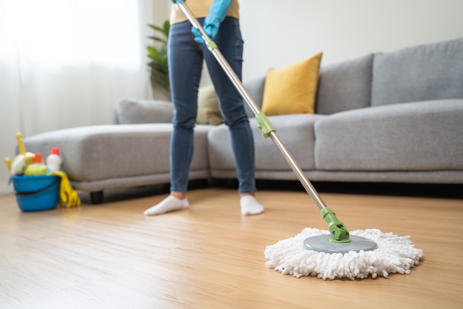 Mopping a wooden floor in a living room with cleaning supplies in the background