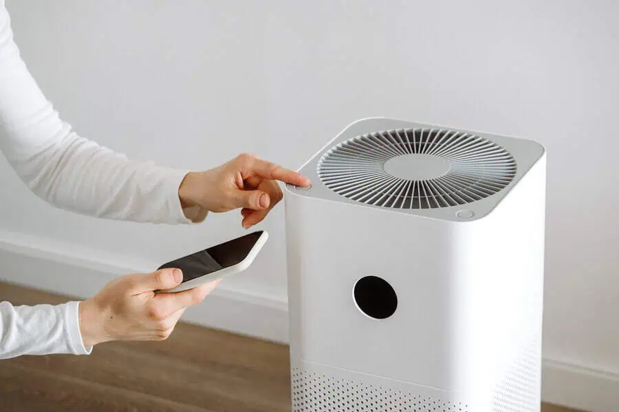 Pressing button on a white air purifier while holding a smartphone