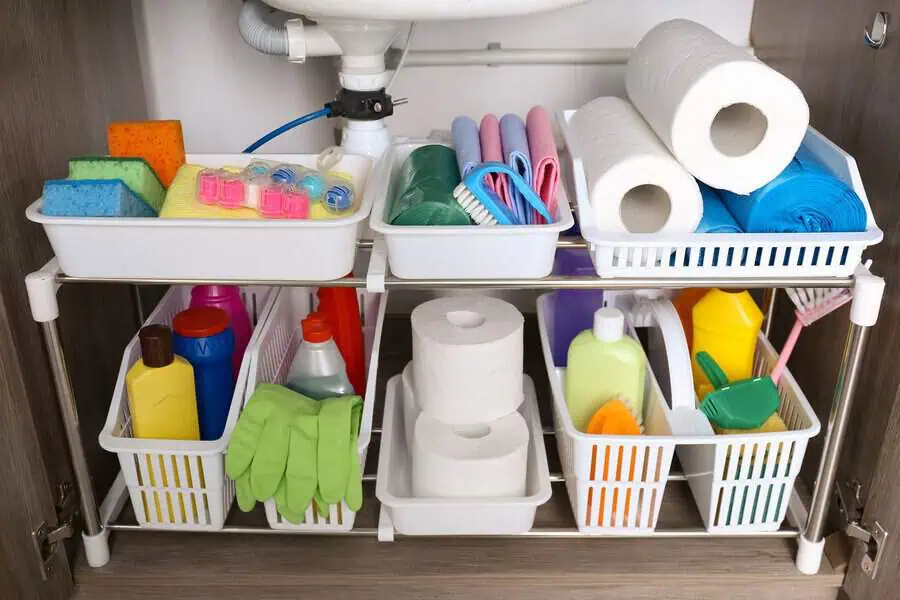 Organized shelves under a sink filled with various cleaning supplies and paper towels