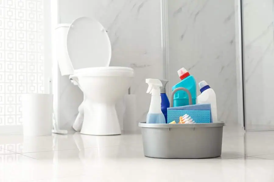 Cleaning supplies in a plastic container on the floor of a bathroom with a toilet in the background