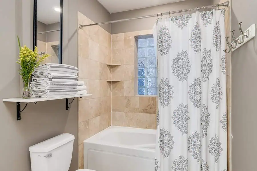 Modern bathroom with a bathtub, floral shower curtain, shelves, and neatly stacked towels