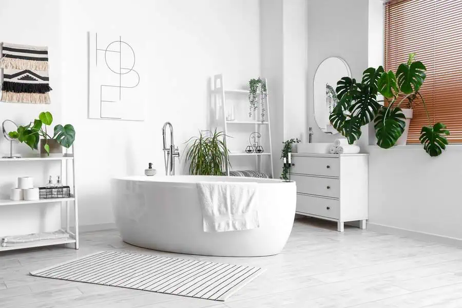 Modern white bathroom featuring a bathtub, plants, a vanity, and wall art