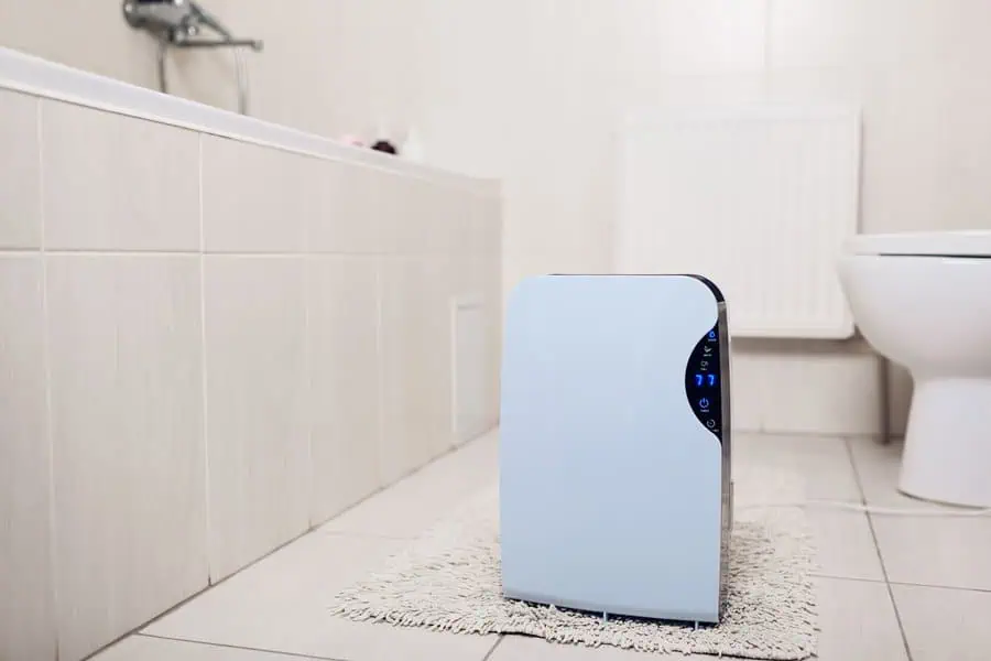 Portable dehumidifier on a small rug in a tiled bathroom near a bathtub and toilet