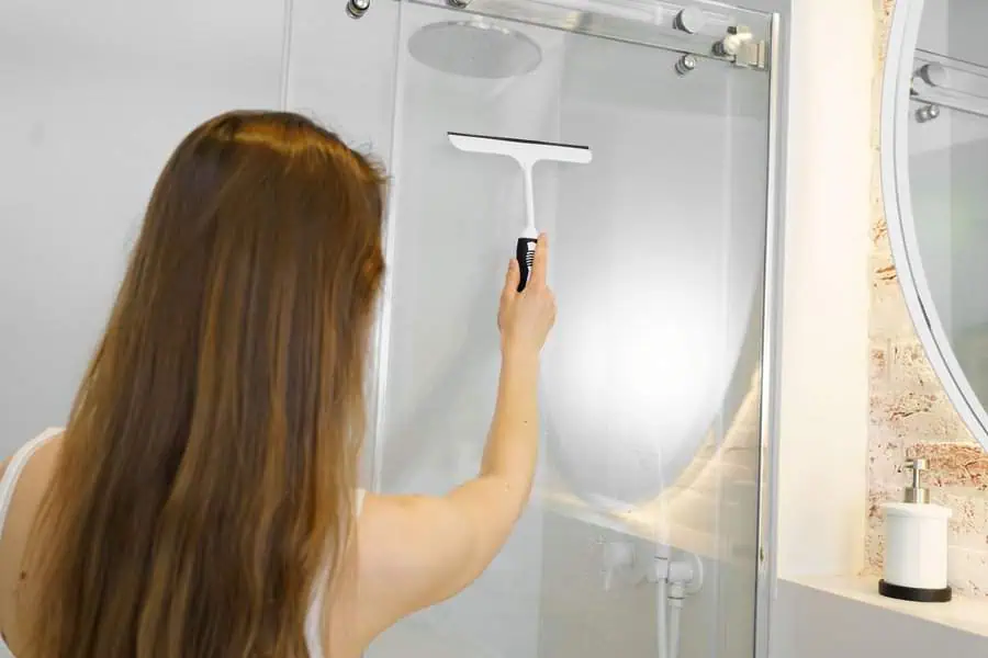 Cleaning a shower glass door with a squeegee in a modern bathroom