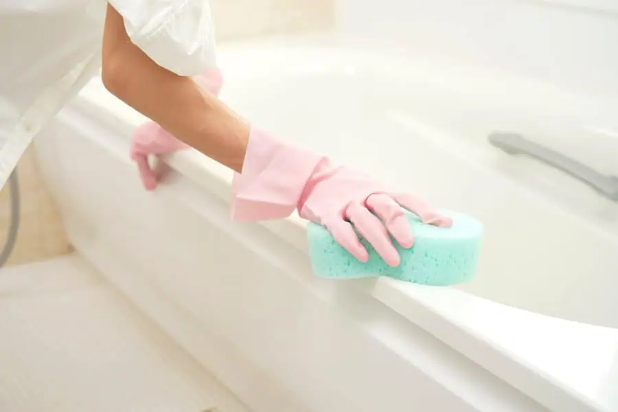 Wearing pink gloves and cleaning a bathtub with a blue sponge