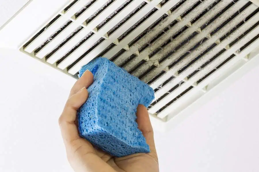 Hand using a blue sponge to clean a dirty air vent