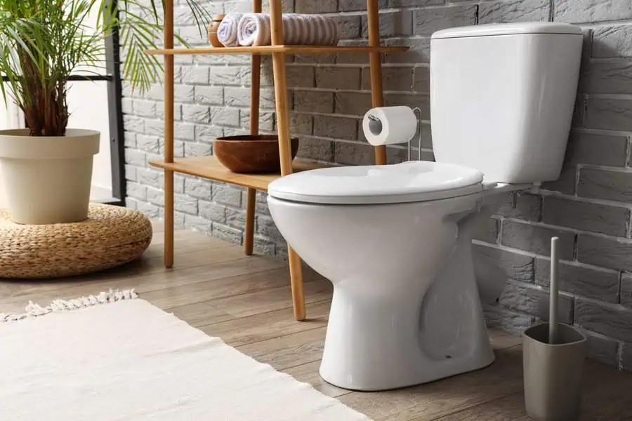 Modern bathroom with white toilet, gray brick wall, and wooden shelving