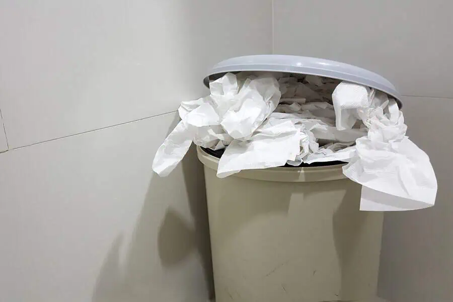 A trash can overflowing with crumpled paper in a corner of a room