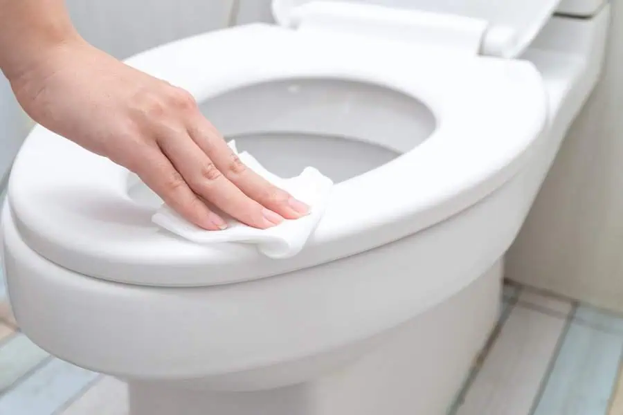 Hand wiping a toilet seat with a tissue in a bathroom