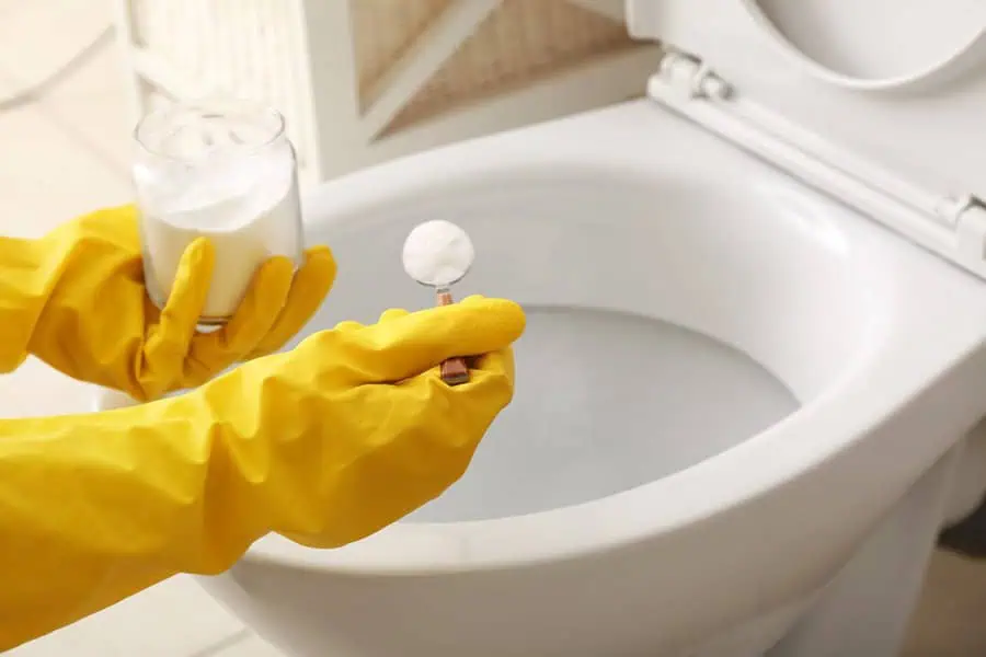 Wearing yellow gloves while cleaning a toilet using a spoonful of white powder