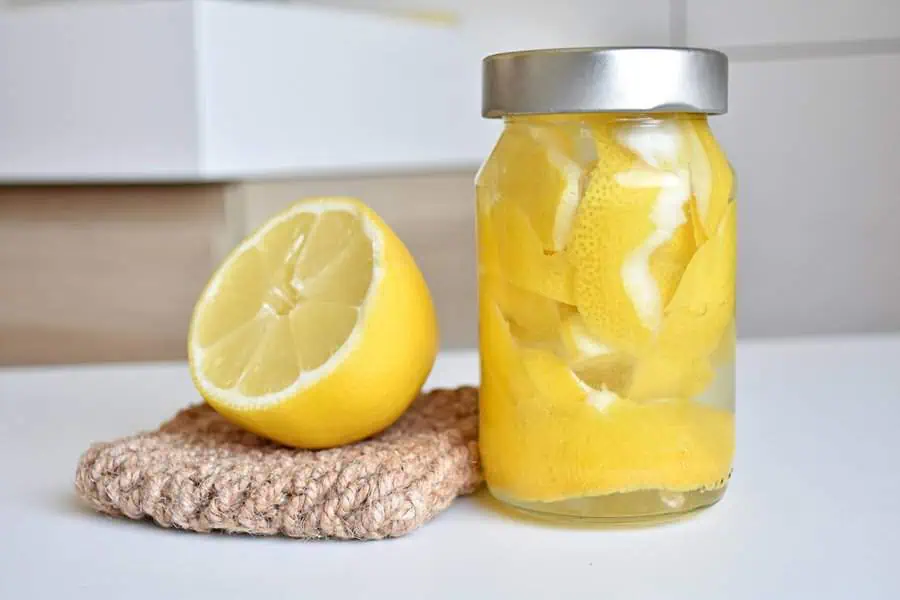 Half lemon and a jar of lemon peels on a beige pad with a blurred background