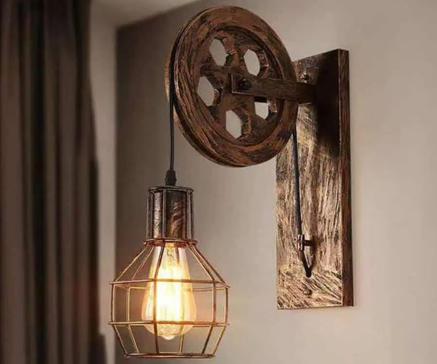 Wall-mounted light fixture with an industrial design featuring a pulley and an exposed bulb encased in a metal cage