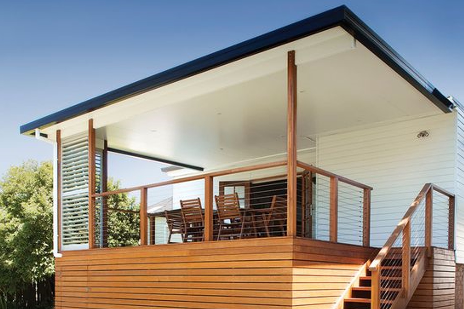 Modern wooden deck with seating area and stairs, attached to a white house