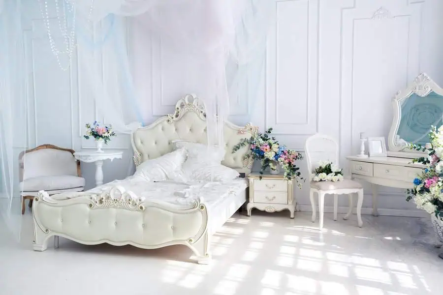 Luxurious bedroom with an ornate bed, delicate drapes, floral decorations, and elegant vintage furniture.