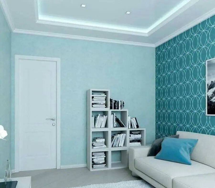 Living room with teal walls, white door, bookshelf, and beige sofa with blue pillow