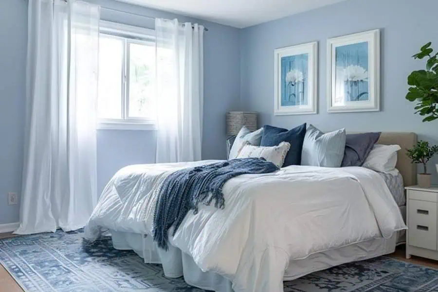 A cozy blue and white bedroom with a neatly made bed and a sunlit window