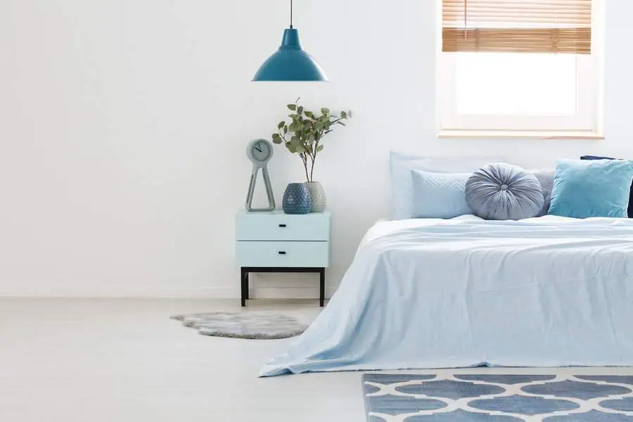 Minimalist bedroom in blue theme featuring a bedside table, modern decor, pendant lamp, and window