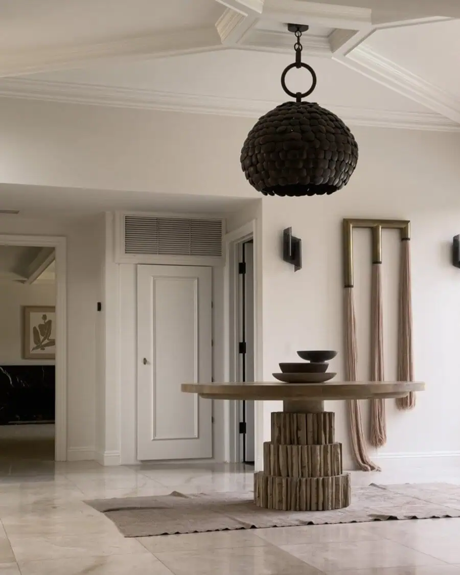 Minimalist entryway featuring a round wooden table with ceramic bowls, modern decor, and a large pendant light