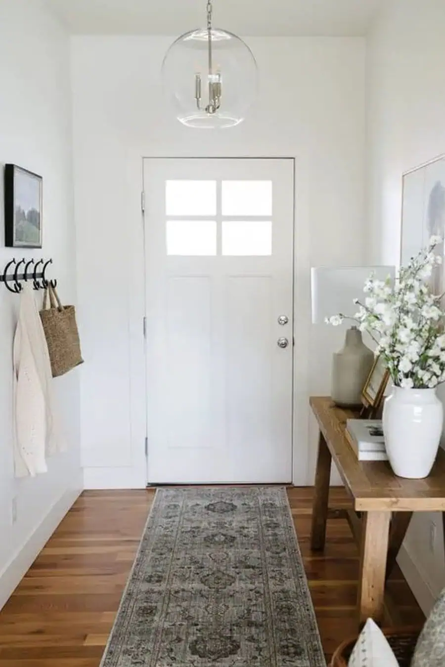 A cozy entryway with a clear glass pendant light providing bright, even illumination over a wooden console table and a patterned runner rug.