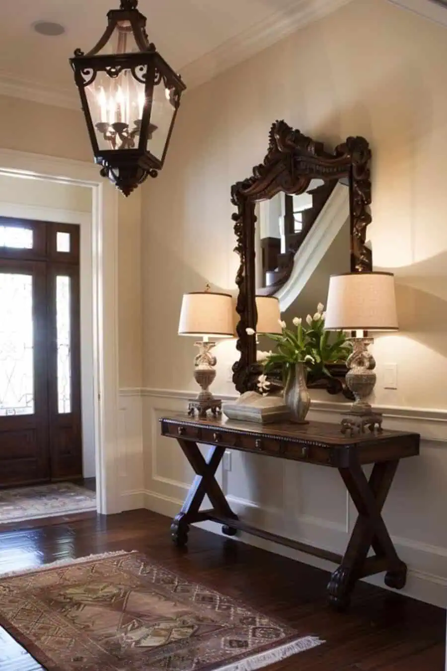 Elegant entryway with ornate mirror, wooden console table, twin lamps, and a large hanging lantern near the front door