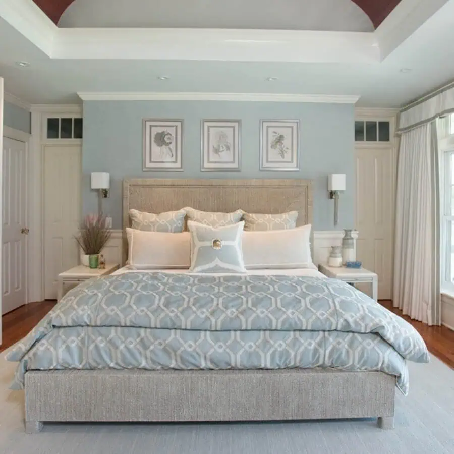 A serene bedroom with light blue walls, patterned bedding, and three framed artworks above the bed