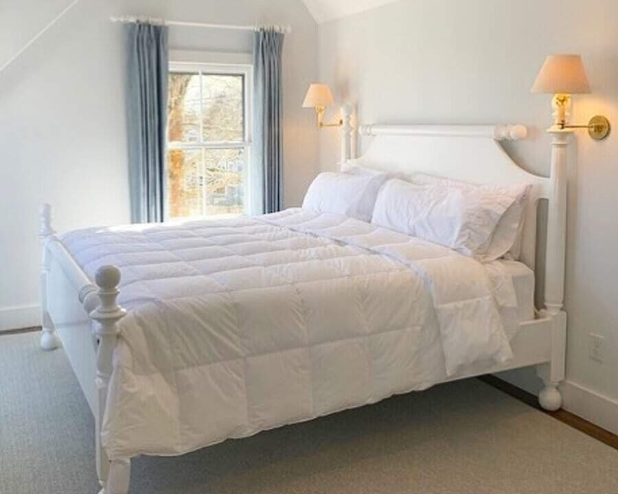 Cozy bedroom with a white wooden bed, plush bedding, and natural light from a small window.