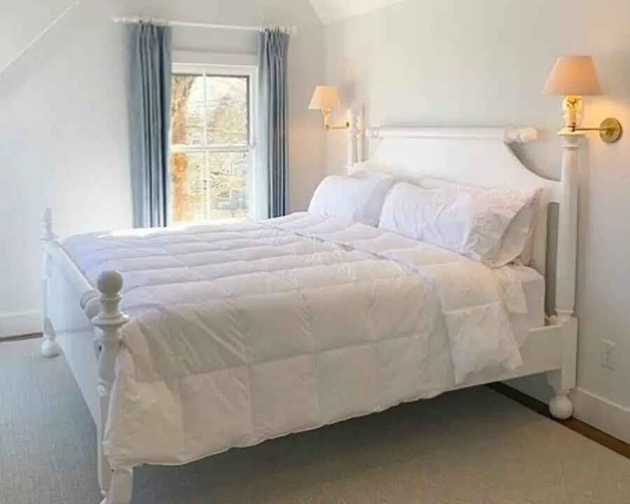 Cozy bedroom with a white wooden bed, plush bedding, and natural light from a small window.