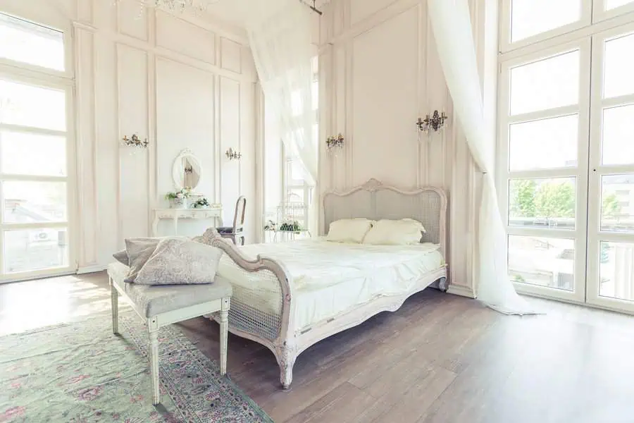 Bright vintage bedroom with large windows, a classic bed, soft drapes, and an elegant vanity table.