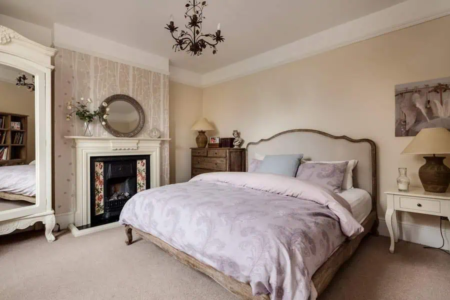 Cozy bedroom with vintage decor featuring a king size bed with tidy done bedding, a fireplace, and an ornate mirror above it