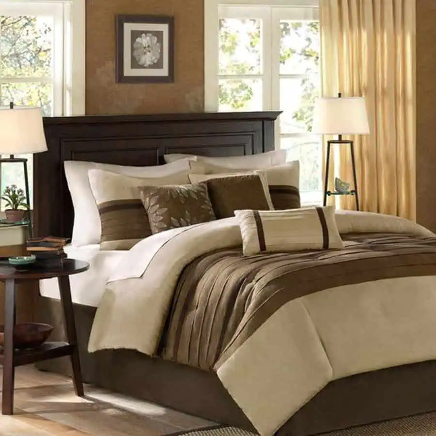 A cozy bedroom with a neatly made bed featuring brown and beige bedding, lamps, and a nightstand.