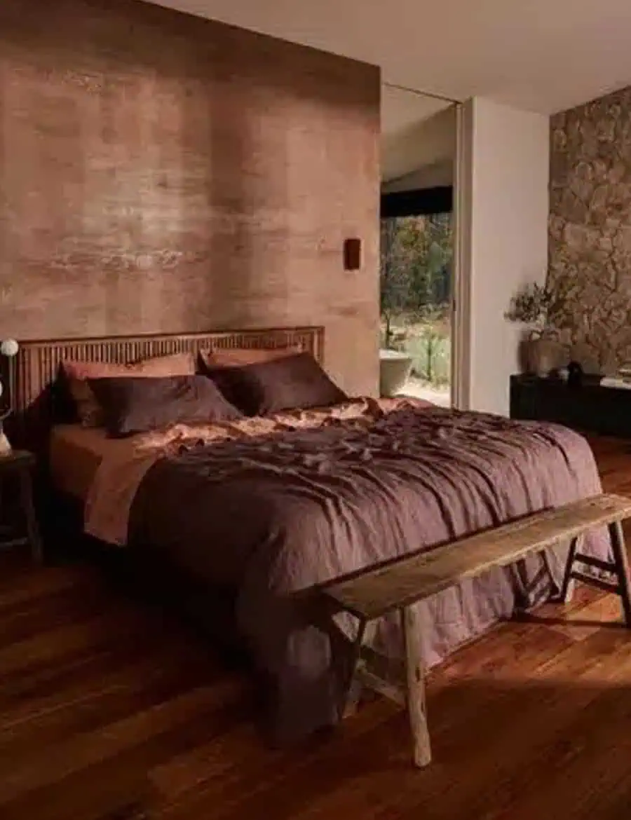 Bedroom with a rustic, cozy style featuring a wooden bed frame, wooden bench, and a stone accent wall.