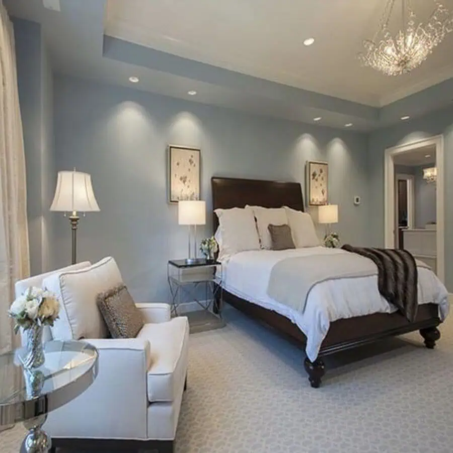 Elegant bedroom featuring a large bed, armchair, nightstands, lamps, and soft blue walls