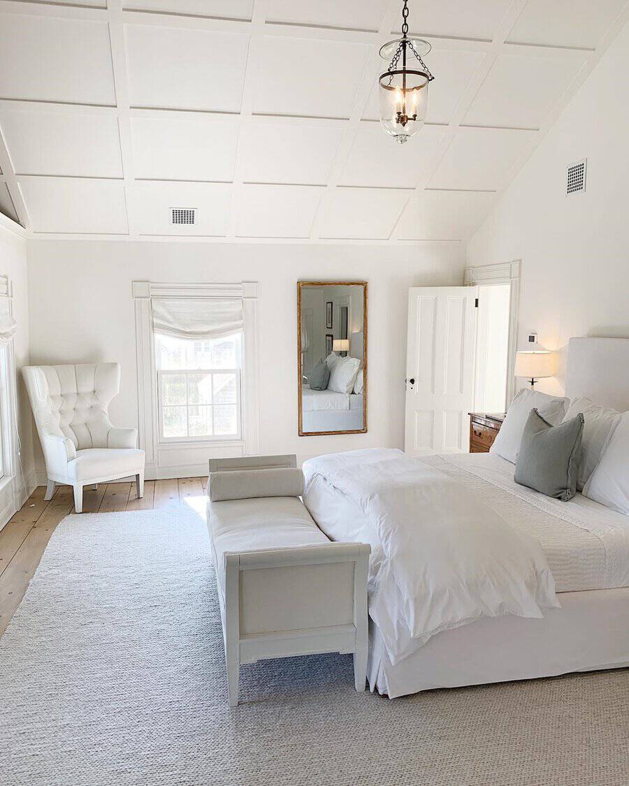 Bright, airy bedroom with white furniture, a large mirror, and a tufted armchair, creating a serene atmosphere.